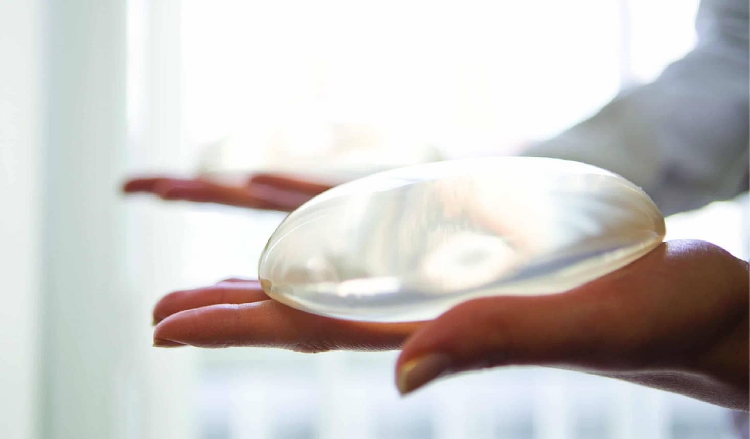 A person holding a breast implant, showcasing the surgical implant used in breast augmentation procedures.
